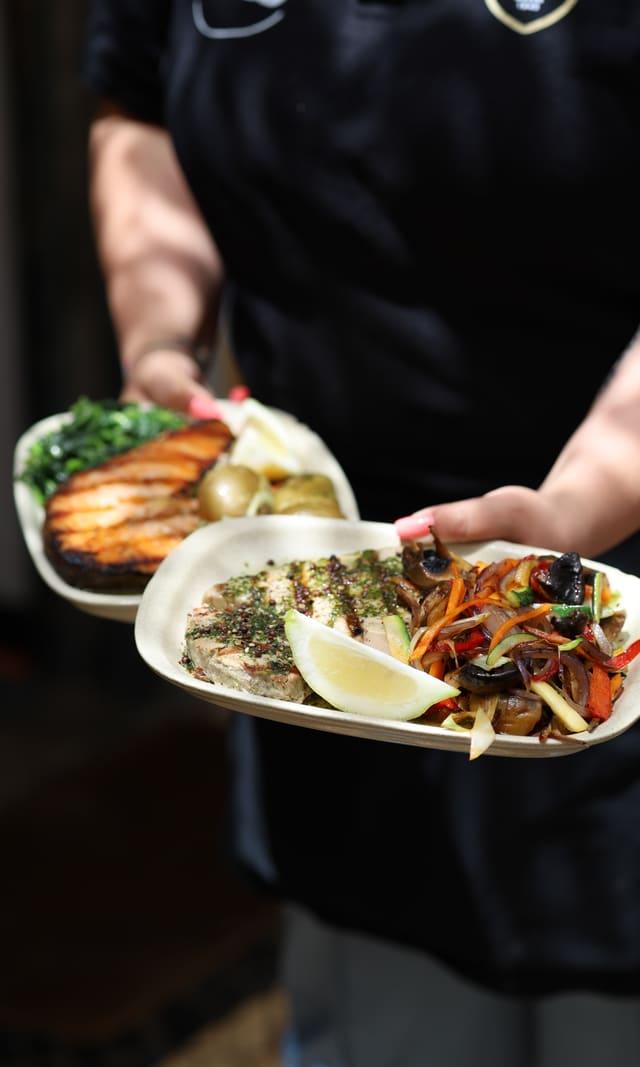 Waiter carrying two plates of fish with vegetables